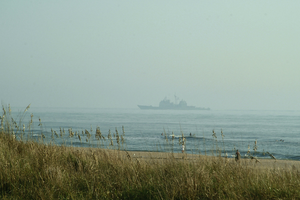 As Virginia Beach Surfers Catch The Morning Beach Break, A Norfolk-based U.s. Navy Warship Returns Home Image